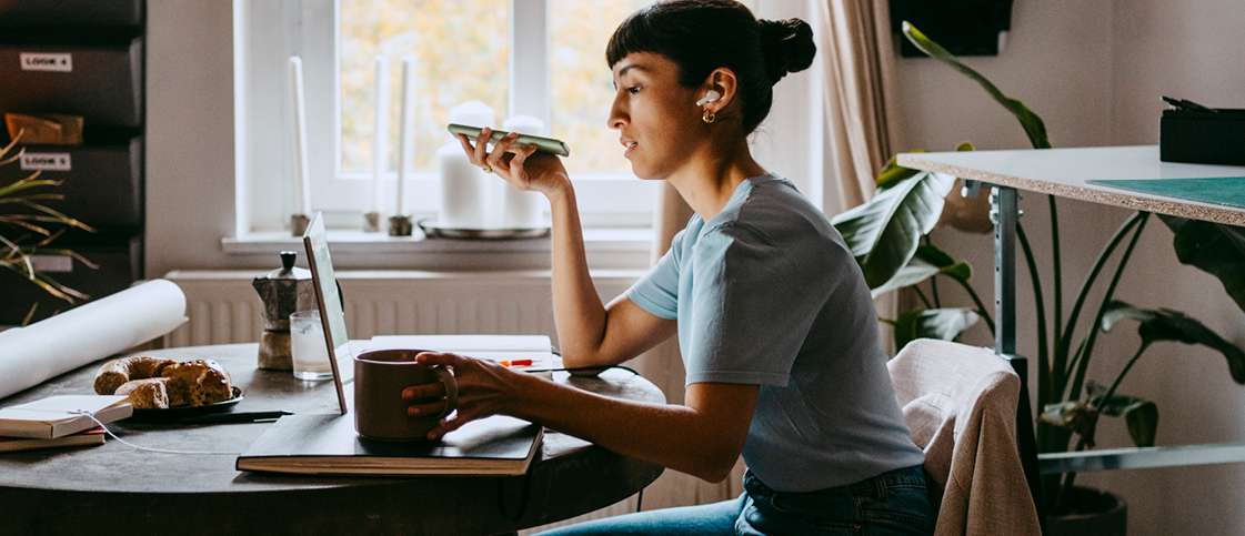 Side view of female freelancer talking on speaker while sitting on chair at home office.