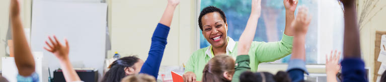 Female teacher smiling and raising her hand along with her students